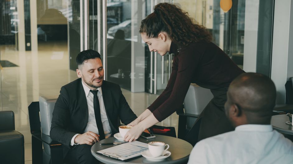 A business meeting in a café as waitress serves coffee to professionals.