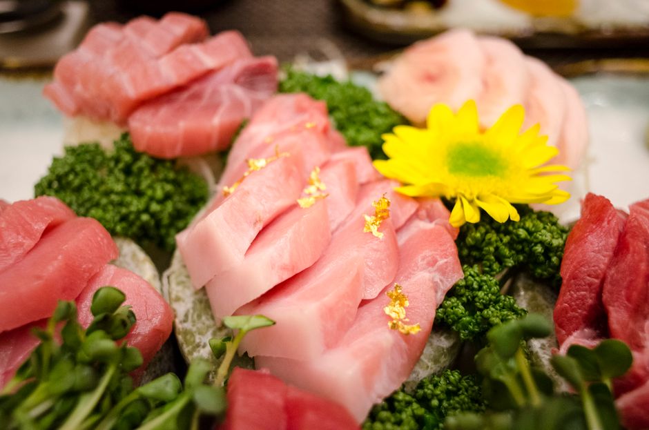 Decorative sushi platter featuring fresh tuna slices, golden leaf accents, and vibrant botanical garnishes.